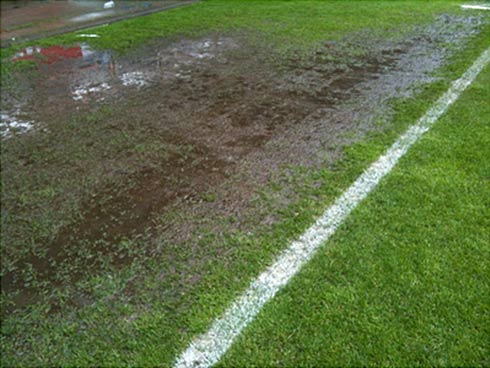 Staunässe im Aufwärmbereich eines Stadionrasens. Folge der Bodenverdichtung durch hohe Belastung.